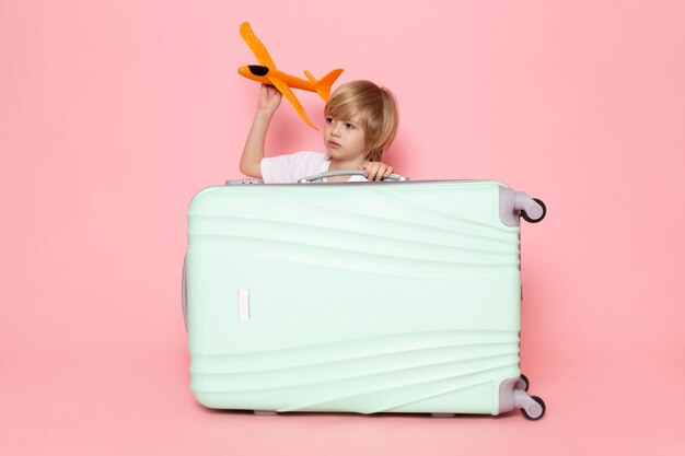 ピンクの机の上にオレンジ色の飛行機を保持している正面金髪の子供