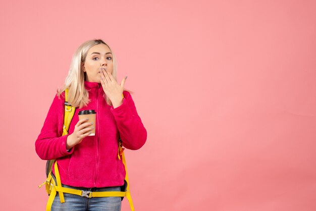 Front view blonde traveler woman with backpack putting hand on her mouth holding coffee cup