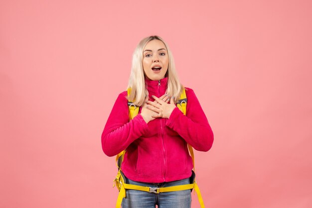 Front view blonde traveler woman with her backpack standing on pink wall