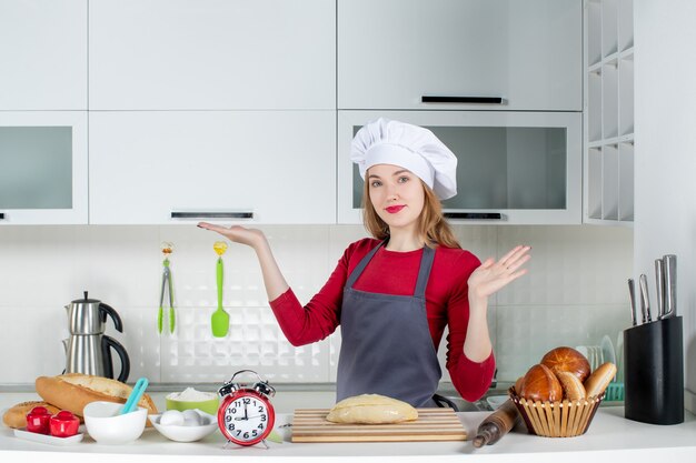 부엌 테이블 뒤에 서 있는 요리사 모자와 앞치마에 전면 보기 금발의 여자