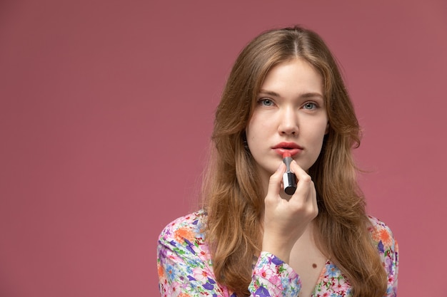 Front view blonde woman uses red lipstick on pink wall