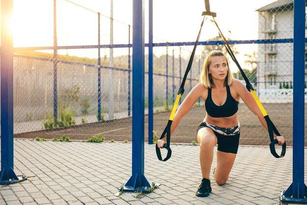 Front view of blonde young woman working out outdoors slim girl wearing sportswear standing on one knee looking aside stretching concept of sporty living and athletics