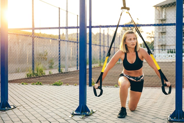 Вид спереди на блондинку, тренирующуюся на открытом воздухе, стройную девушку в спортивной одежде, стоящую на одном колене и смотрящую в сторону, растягивающую концепцию спортивной жизни и легкой атлетики
