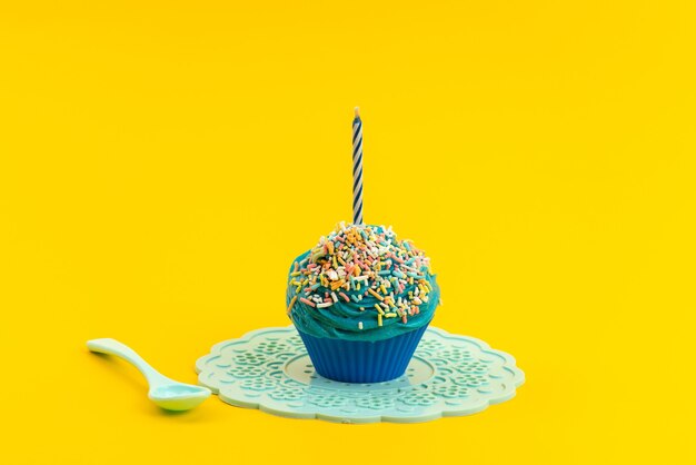 A front view blue cake with candle white, plastic spoon on yellow, biscuit confectionery color