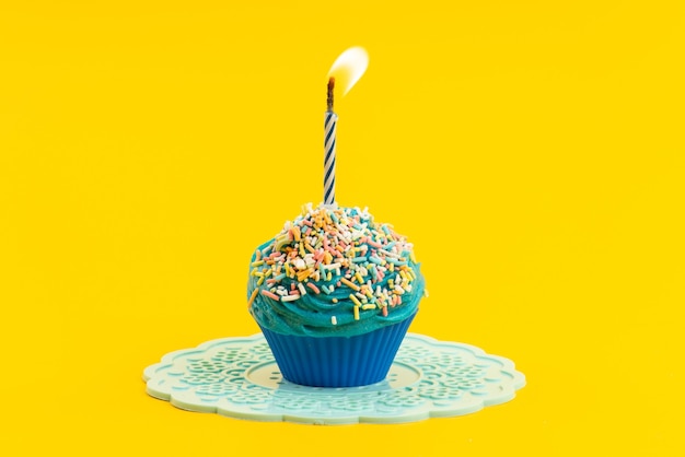 A front view blue cake with colorful little candies and candle on yellow, color biscuit sugar