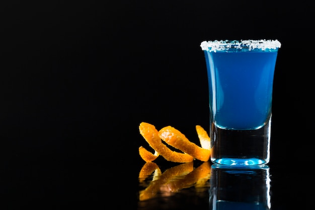 Front view of blue cocktail in shot glass with orange peel