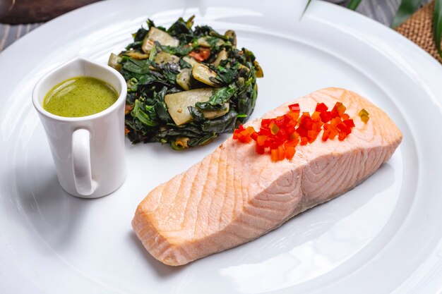 Вид спереди отварной красной рыбы с тушеной зеленью и соусом на тарелке