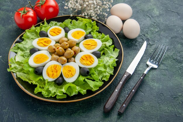 front view boiled sliced eggs with green salad and olives on dark background