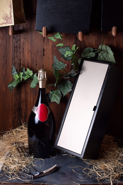 A front view bottle of alcohol black bottle with golden cap along with black box and green leaves on the brown background drink winery alcohol