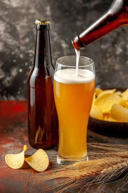 Front view bottle of bear pouring up into the glass with cips on dark background