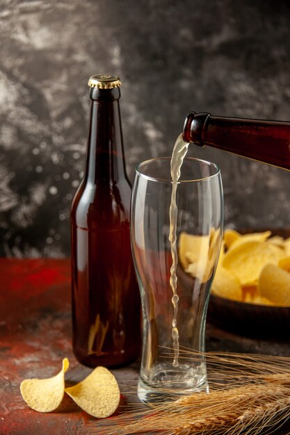 Вид спереди бутылка медведя вливается в стакан с чипсами на темном фоне