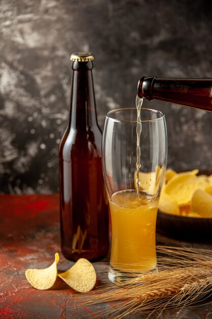 Front view bottle of bear pouring up into the glass with cips on dark desk