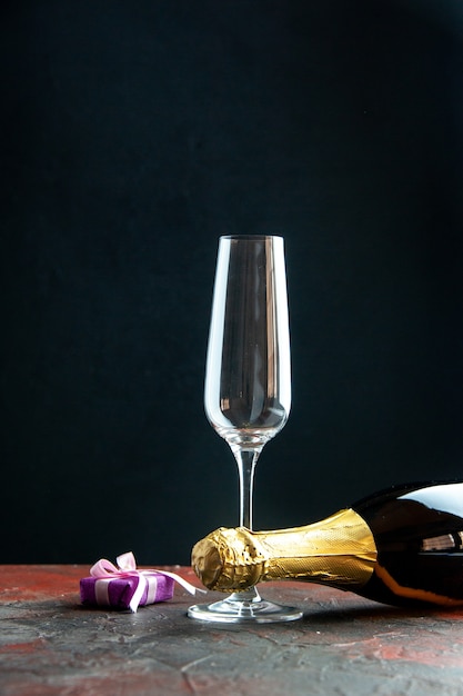 Front view bottle of champagne with wine glass on dark background