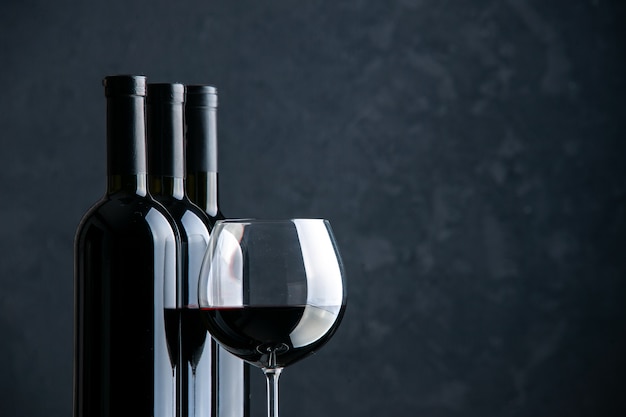 Вид спереди бутылки вина с бокалом вина на темной поверхности
