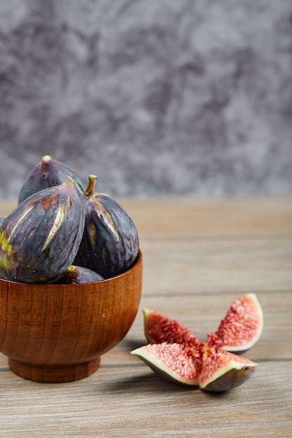 Front view of the bowl of black figs and slices of figs on wooden table.