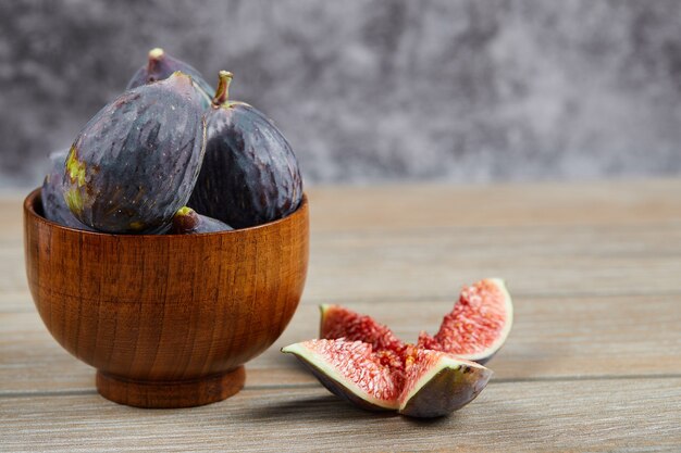 Front view of the bowl of black figs and slices of figs on a wooden table