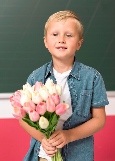 彼の先生のためにいくつかの花を持つ正面少年