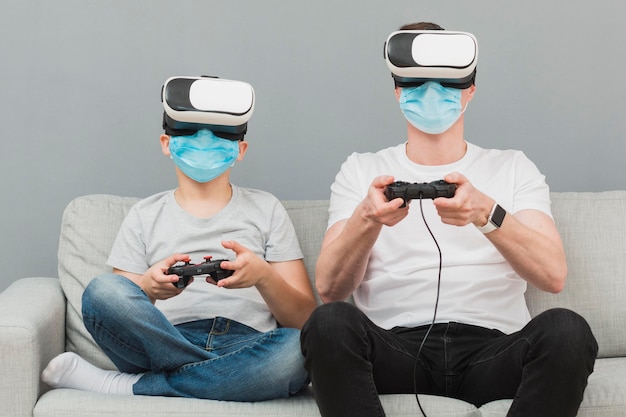 Front view of boy and man playing with virtual reality headset while wearing medical masks