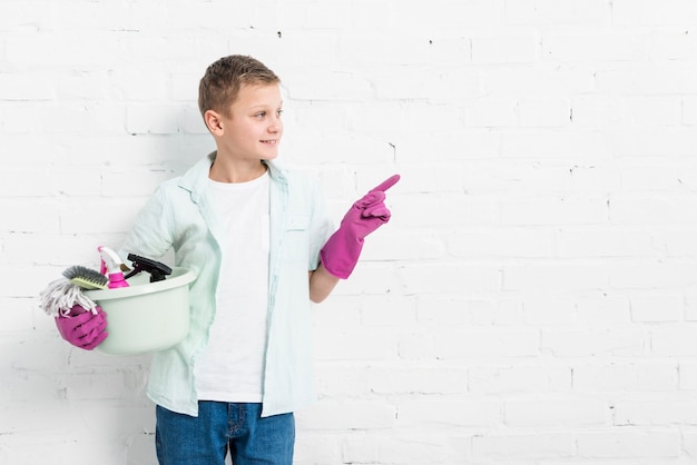 Вид спереди мальчика позирует и указывая, удерживая чистящие средства