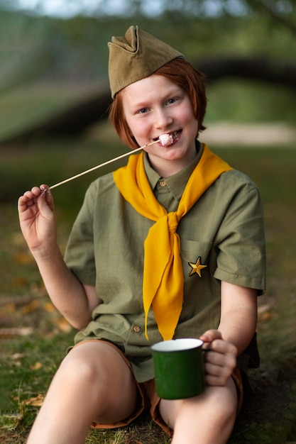 Free photo front view boy scout eating marshmallow