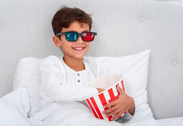 Free photo front view boy with 3d glasses and eating popcorn