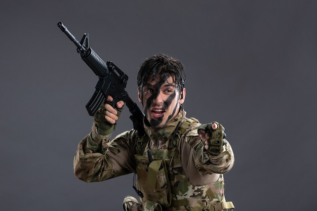 Вид спереди храброго солдата, сражающегося в камуфляже с пулеметом на серой стене