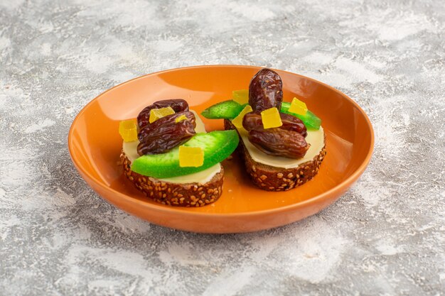 Front view bread toasts with cucumber and dried plums inside orange plate on white surface