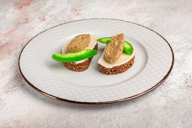 Front view bread toasts with pate and cucumber slices inside plate on white surface