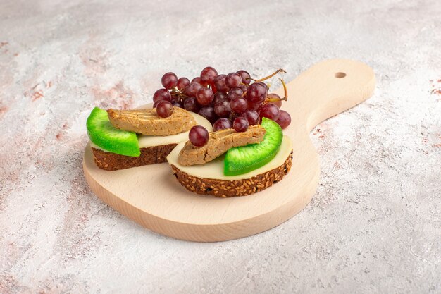 Front view bread toasts with pate grapes and cucumber slices inside plate on white surface