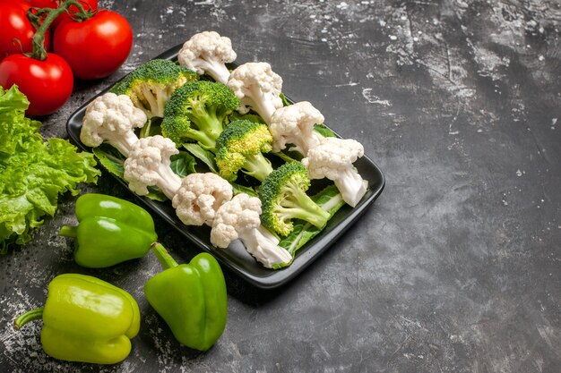 Front view broccoli and cauliflower on black rectangular plate tomatoes green bell peppers lettuce on dark background free place