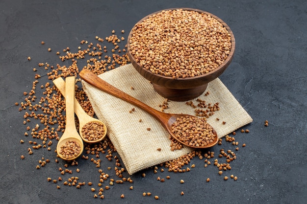 front view brown buckwheat inside plate with pair of spoons on dark background