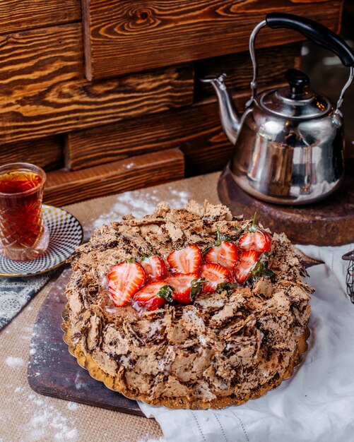 Коричневый шоколадный торт с красной свежей клубникой сверху и горячим чаем на коричневом полу