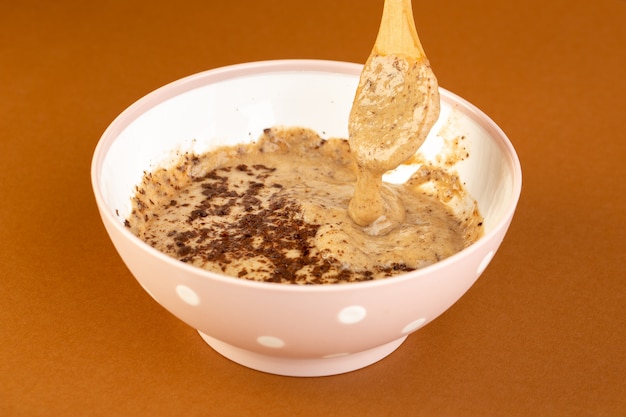 Вид спереди коричневый шоколадный десерт вкусный вкусный сладкий с порошкообразным кофе внутри белой тарелкой, изолированный на фоне молочного кофе