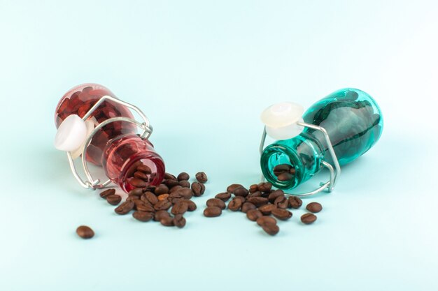 A front view brown coffee seeds inside colored glass jars on the blue surface