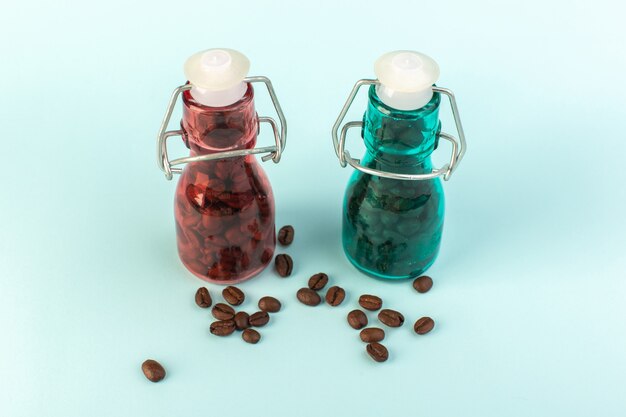 A front view brown coffee seeds inside colored glass jars on the blue surface