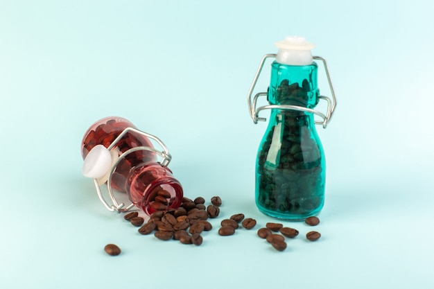 A front view brown coffee seeds inside colored glass jars on the blue surface 