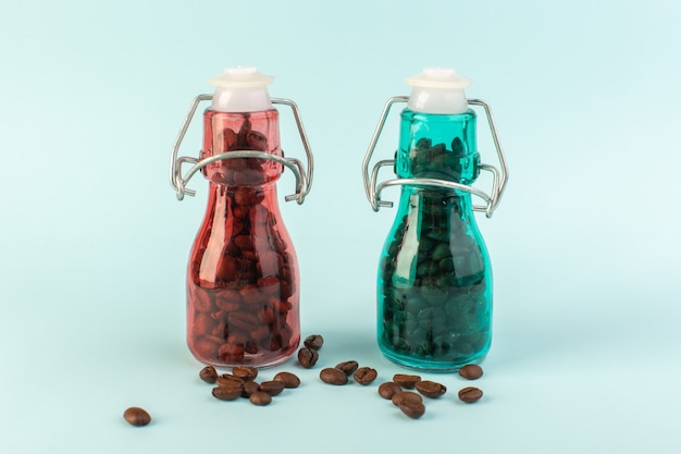 Коричневые семена кофе, вид спереди внутри цветных стеклянных банок на синей поверхности