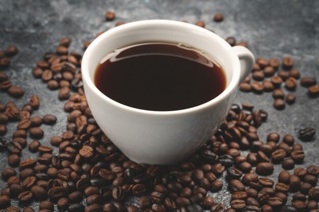 Front view of brown coffee seeds with cup of coffee on dark surface