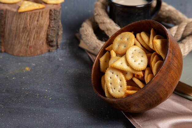 Front view of brown plate with crisps and crackers along with milk on the grey surface