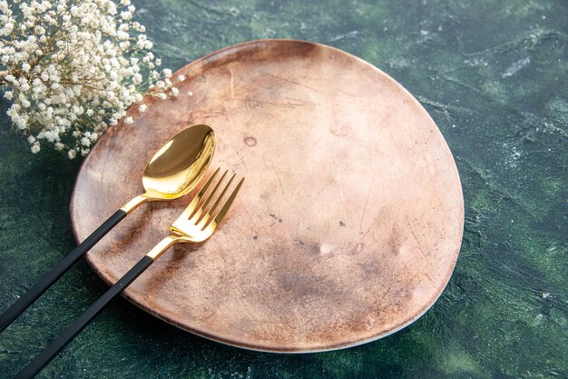 front view brown plate with golden spoon and fork on dark background