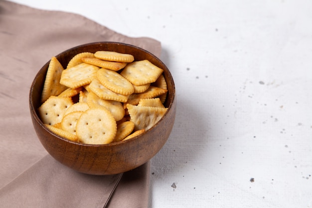 Front view of brown plate with salted tasty crackers and crisps on the light surface