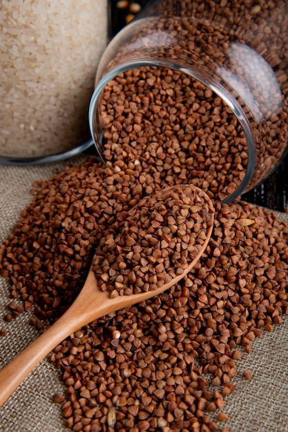 Front view buckwheat scattered from a jar with a wooden spoon and rice on burlap