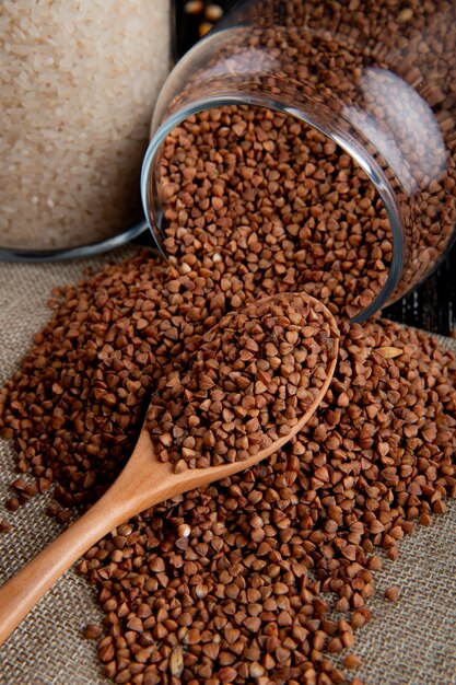 Front view buckwheat scattered from a jar with a wooden spoon and rice on burlap