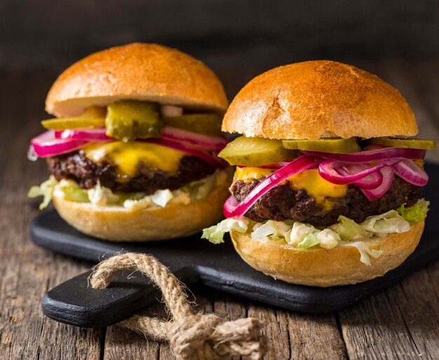 Front view burgers with pickles and red onions on cutting board