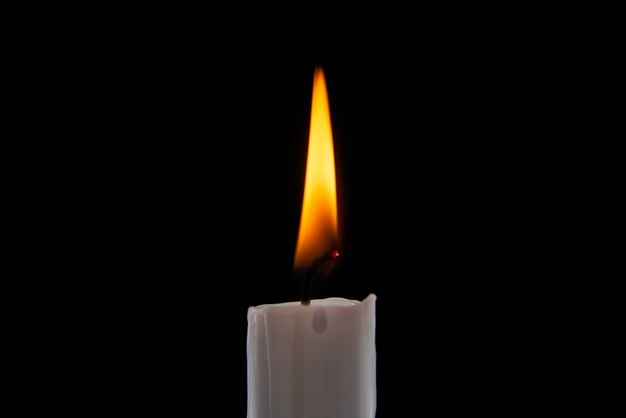 Вид спереди горящей свечи на темной поверхности