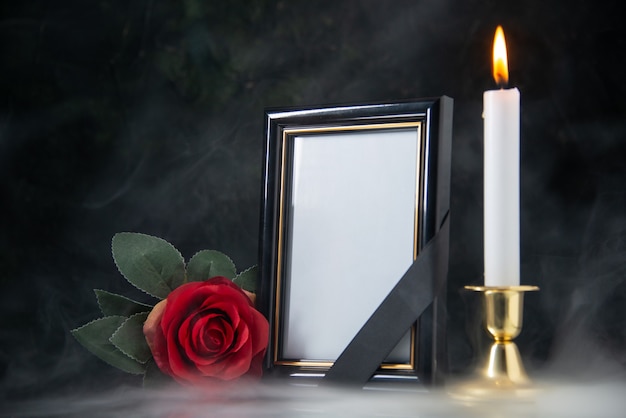 Front view of burning candle with picture frame on a black surface