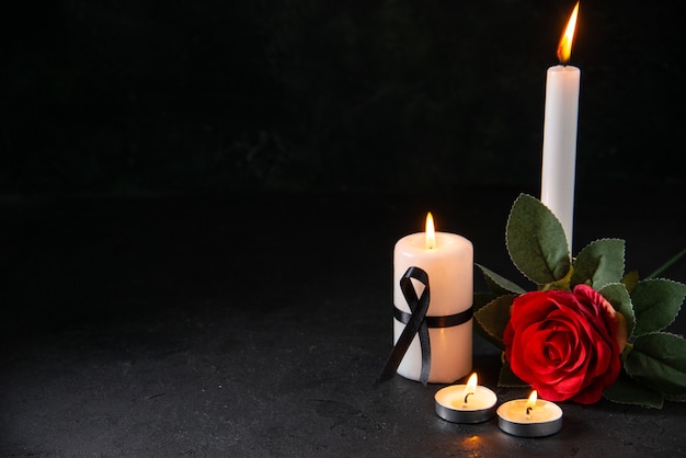 Front view of burning candle with red flower on dark surface