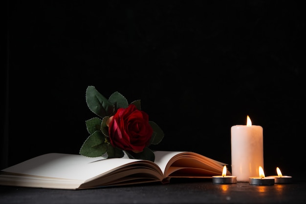 Front view of burning candles with open book and red flower on a dark surface