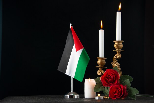 Front view of burning candles with palestinian flag on a dark surface