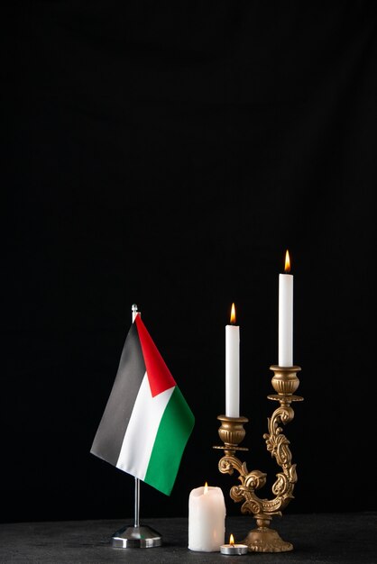 Front view of burning candles with palestinian flag on dark surface